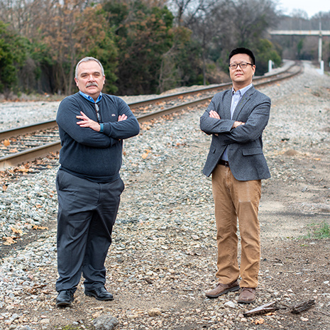 Qian and Rizos pose in front of railroad tracks
